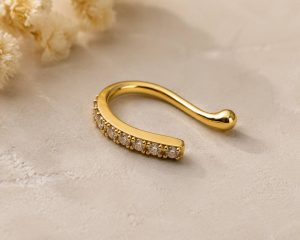 پیرسینگ فیک بینی طلایی با ردیف نگین‌های شفاف روی بدنه خمیده