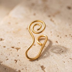پیرسینگ بینی فیک طلایی با طراحی مارپیچ ظریف روی پس‌زمینه سنگی روشن