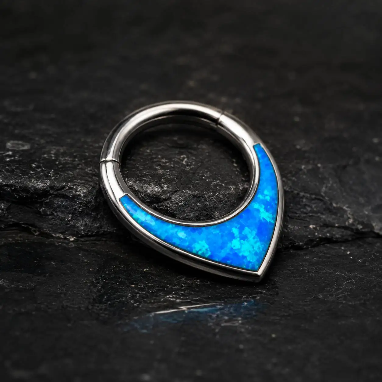 blue-opal-septum-piercing-dark-stone-background نمای نزدیک پیرسینگ سپتوم اوپال آبی مدل اشکی با بدنه نقرهای براق