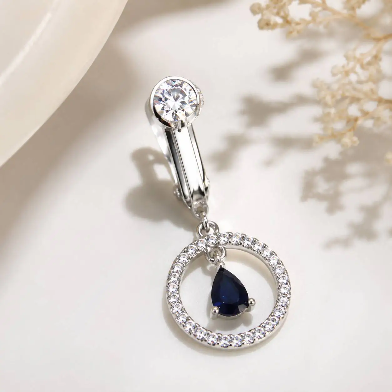blue-teardrop-fake-navel-piercing-product پیرسینگ فیک ناف نقرهای با نگین شفاف و آویز اشکی سرمهای روی پس زمینه روشن
