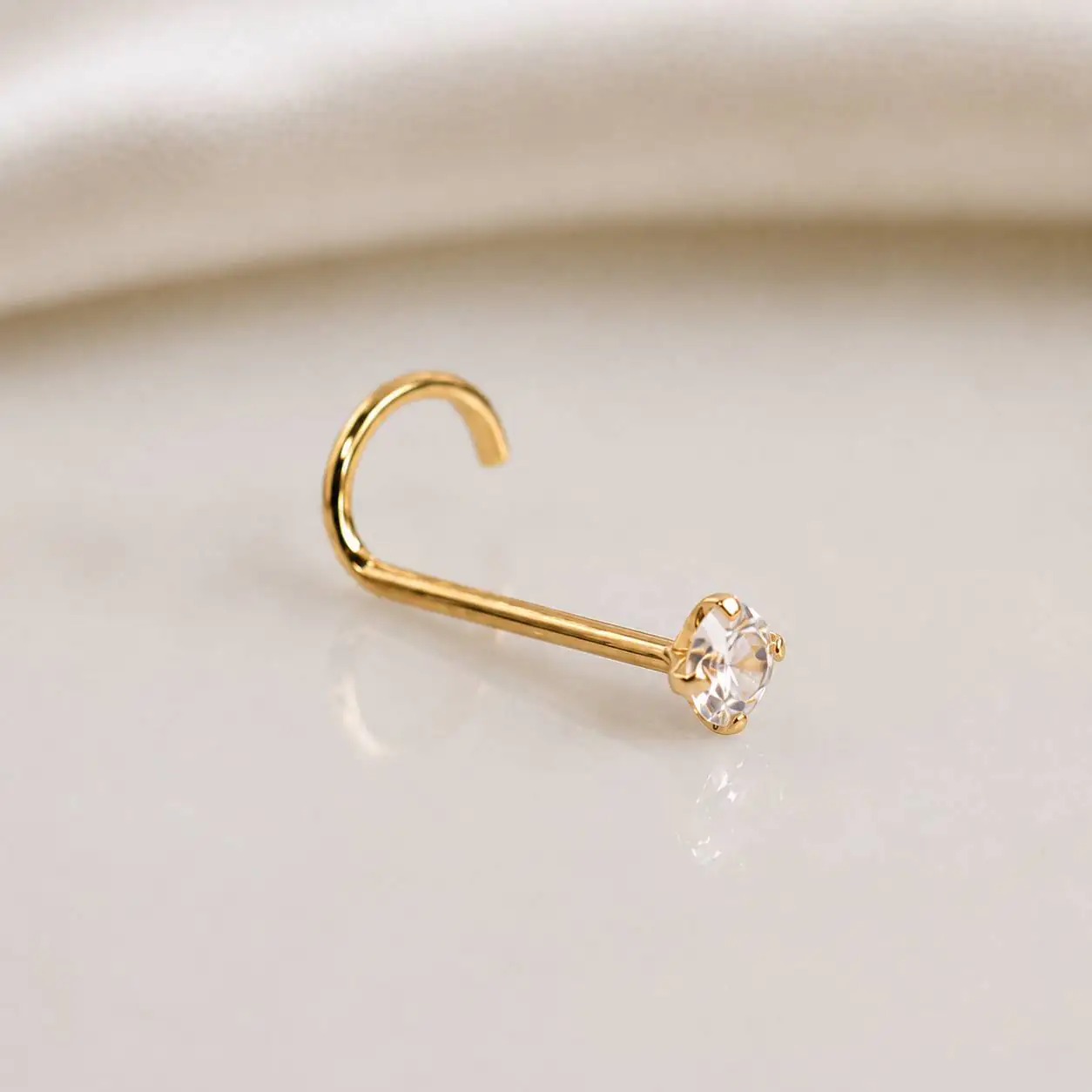 gold-curved-nose-stud-soft-background پیرسینگ بینی طلایی خمیده با نگین براق روی پسزمینه روشن و لطیف