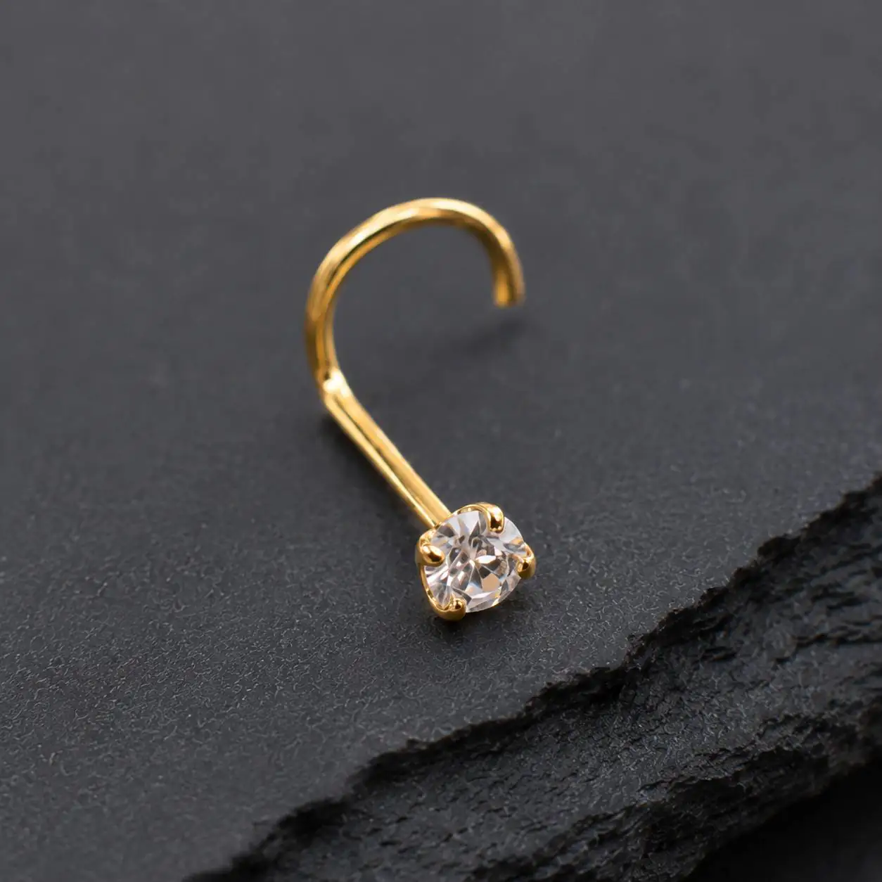 gold-gem-nose-piercing-black-stone پیرسینگ بینی طلایی با نگین شفاف روی پسزمینه سنگی مشکی