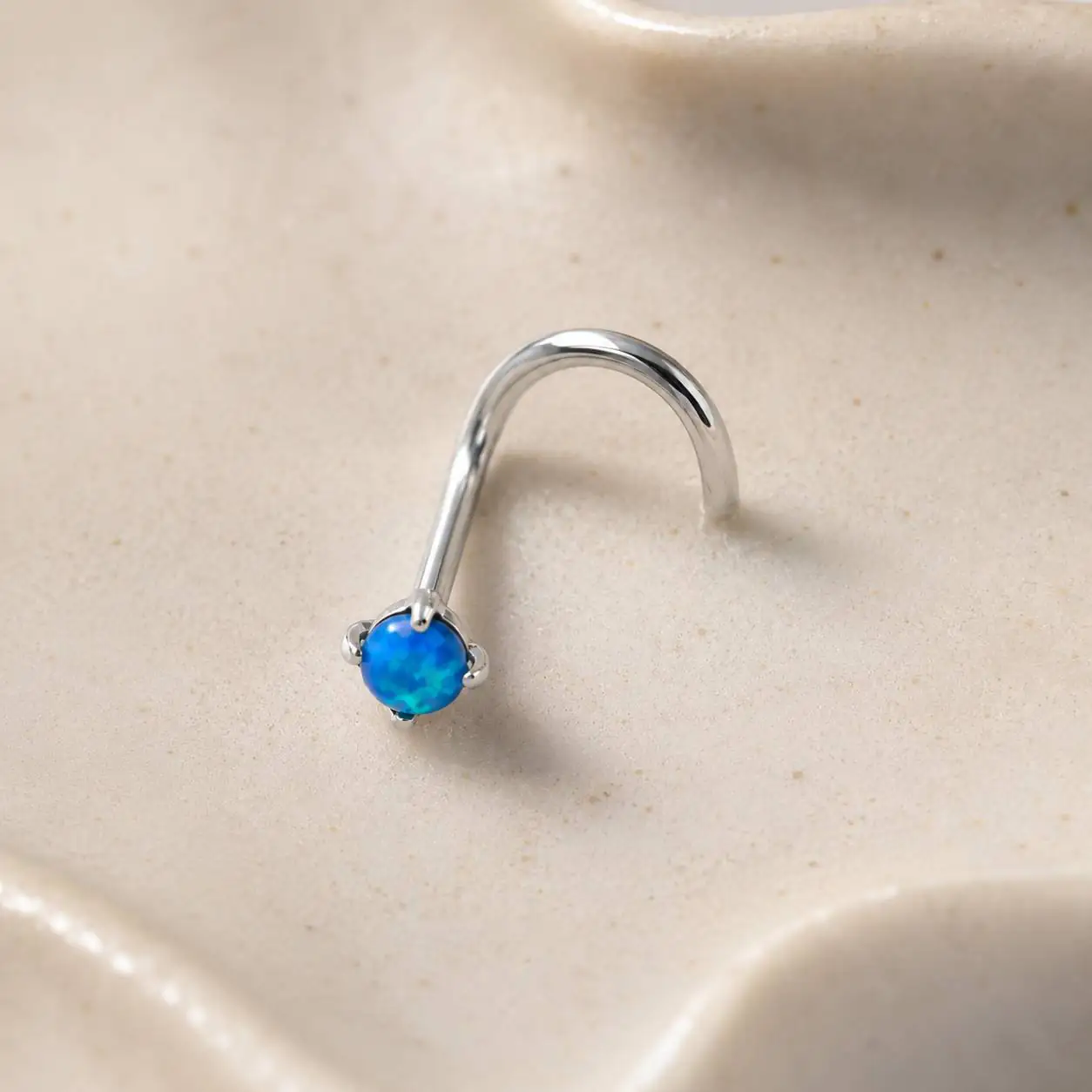 minimal-silver-nose-ring-blue-opal پیرسینگ بینی نقرهای با نگین اوپال آبی روی پسزمینه روشن و مینیمال