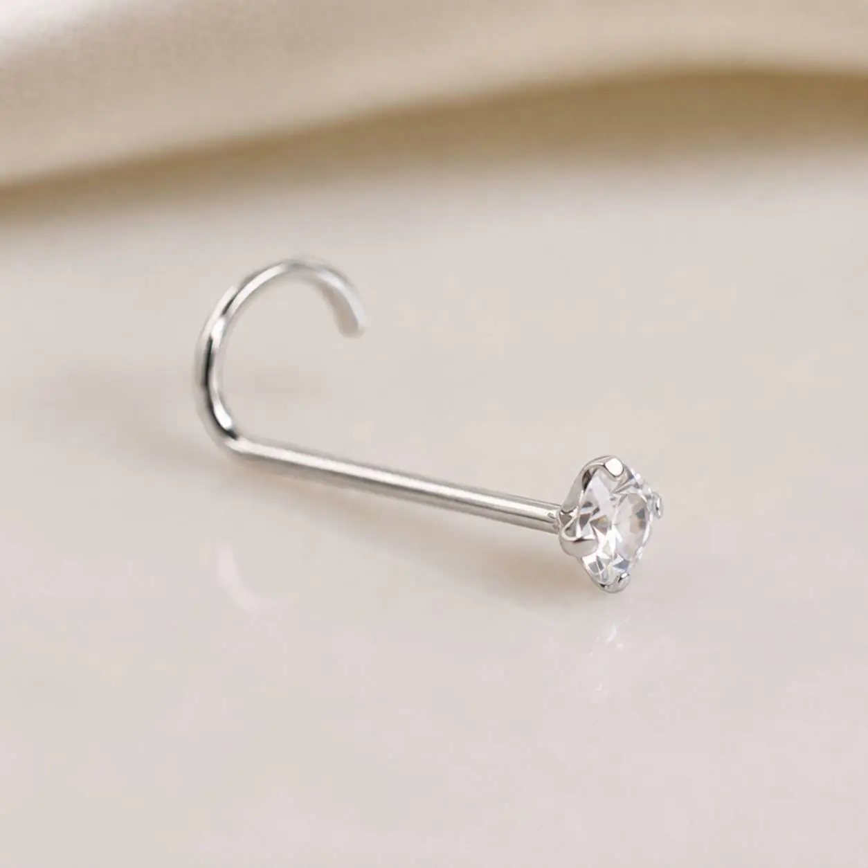 silver-crystal-nose-stud-on-skin عکس محصول پیرسینگ بینی خمیده با نگین شفاف در پسزمینه روشن