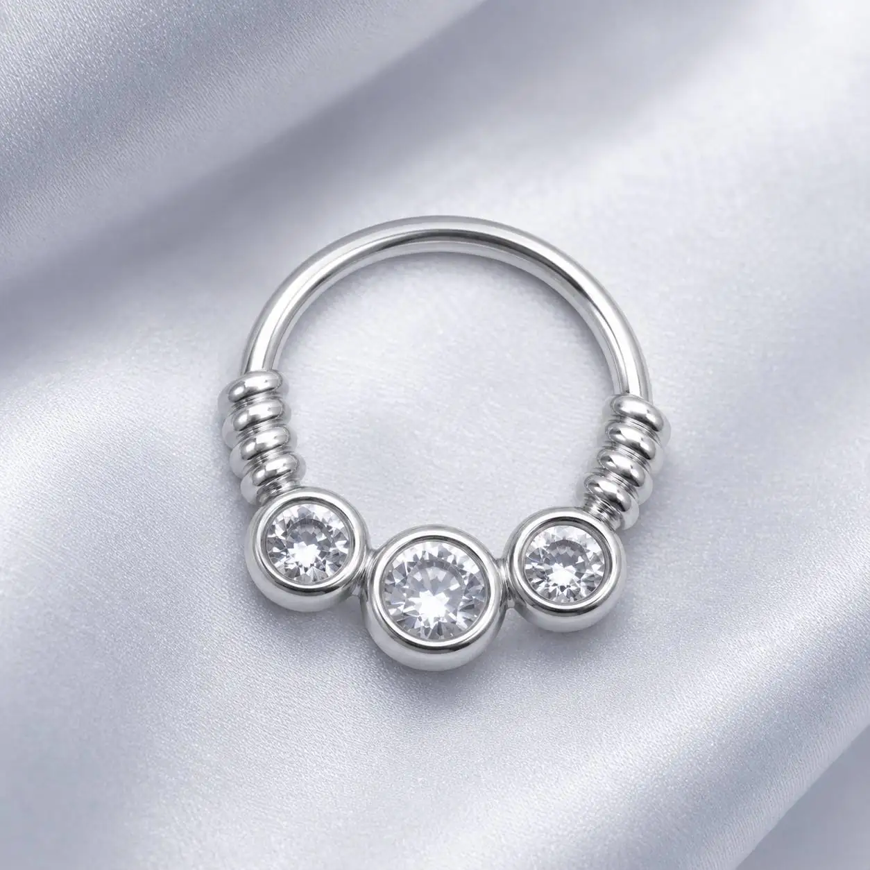 silver-gemstone-septum-piercing-satin-background پیرسینگ سپتوم سه نگین نقرهای با نگین وسط بزرگتر روی پسزمینه ساتن روشن