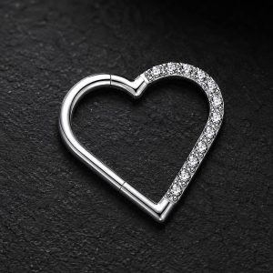 تصویر پیرسینگ سپتوم قلبی نقره‌ای نگین‌دار روی پس‌زمینه بژ با نورپردازی لوکس