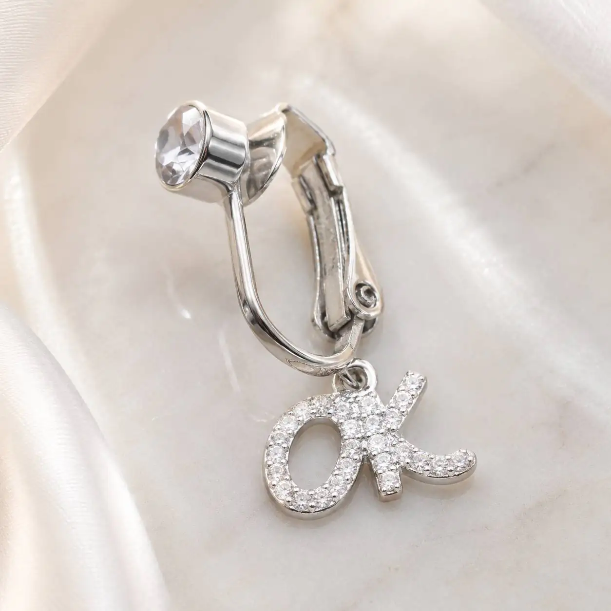 silver-ok-charm-fake-navel-piercing-satin پیرسینگ فیک ناف نقرهای طرح OK روی پسزمینه ساتن روشن