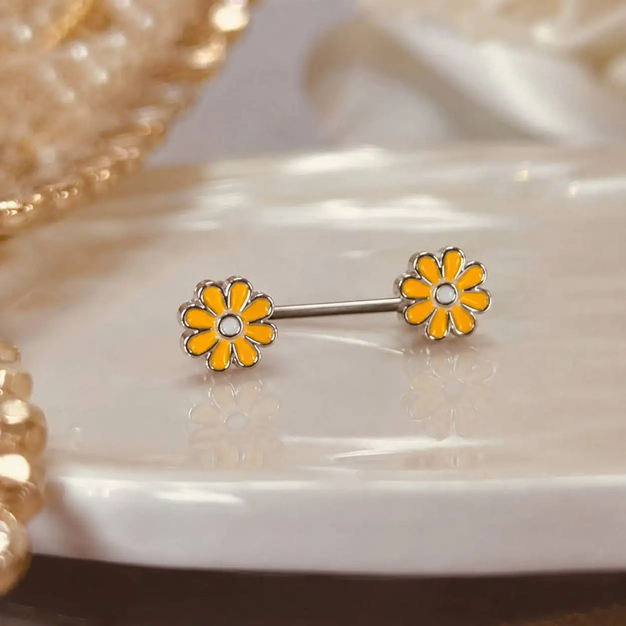 yellow-daisy-nipple-barbell-closeup.jpg نمای نزدیک پیرسینگ نیپل گل زرد با طراحی ظریف گلبرگها