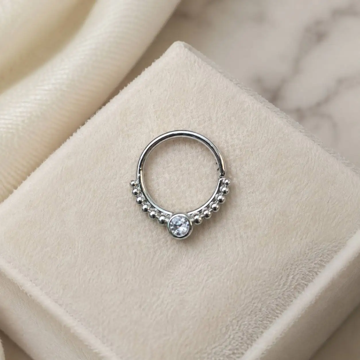 beaded-septum-piercing-marble-background پیرسینگ سپتوم نقرهای با نگین کریستالی روی سنگ مرمر سفید