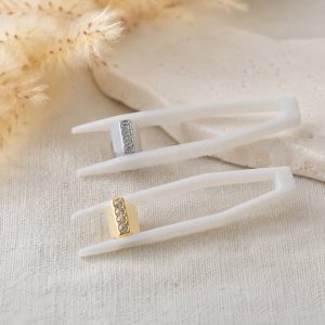 پیرسینگ دندان پنج نگین طلایی و نقره‌ای با پایه سفید روی پس‌زمینه کرم