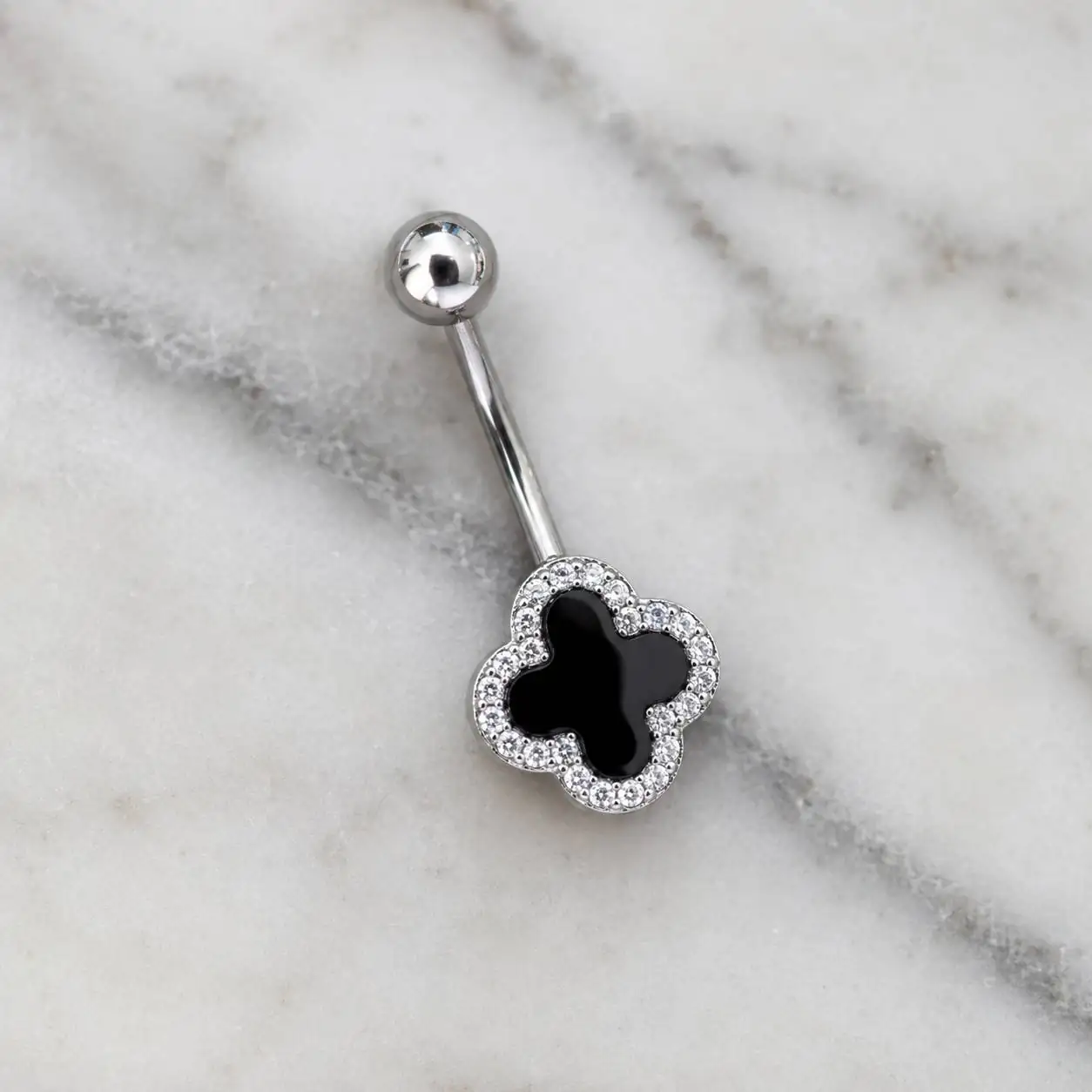 black-clover-navel-jewelry-marble پیرسینگ ناف نگیندار طرح شبدر مشکی روی پسزمینه سنگ مرمر