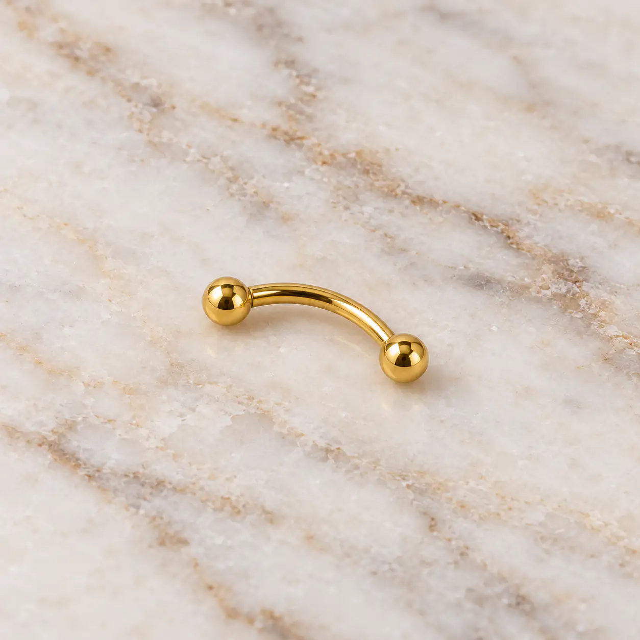 gold-curved-eyebrow-barbell-marble.web پیرسینگ ابرو طلایی ساده با میله منحنی روی سنگ مرمر