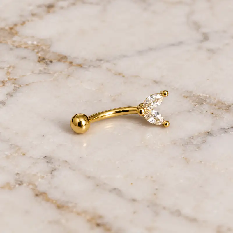 پیرسینگ ابرو طلایی نگین‌دار روی پس زمینه سنگ مرمر سفید