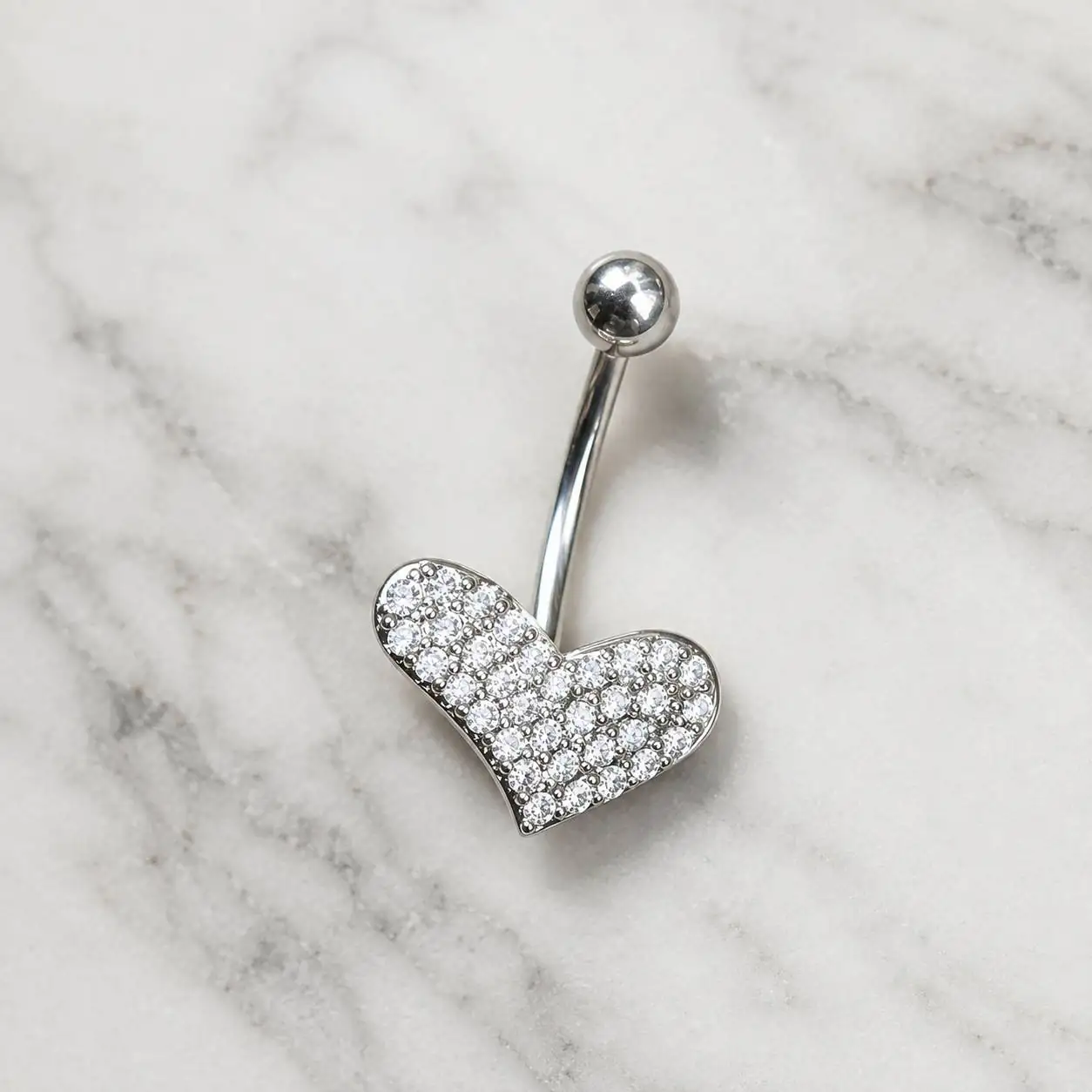 silver-heart-belly-piercing-marble پیرسینگ ناف طرح قلب پرنگین روی پسزمینه سنگ مرمر