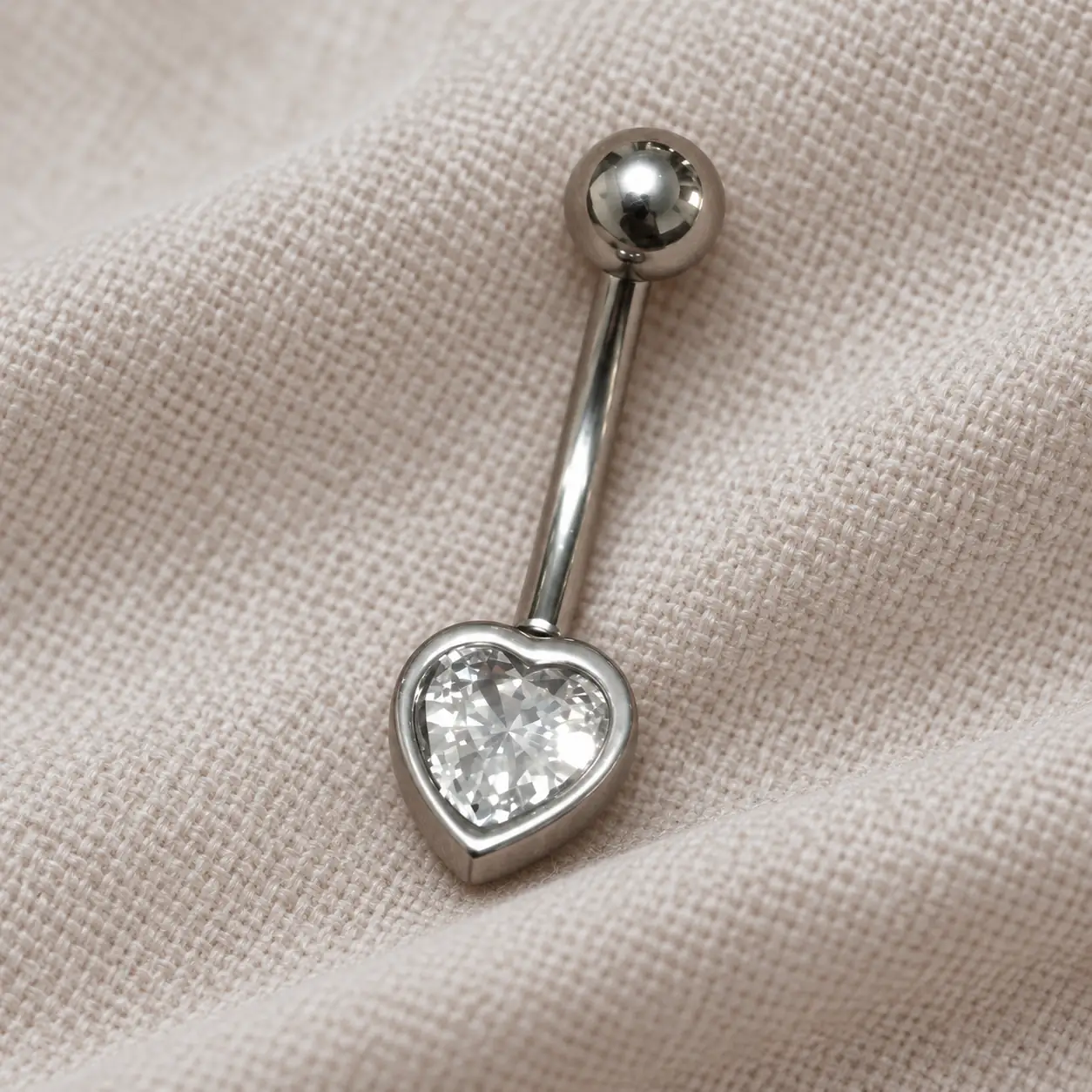 heart-gem-belly-piercing-cotton نمای نزدیک پیرسینگ ناف نگیندار قلبی روی پارچه نخی روشن